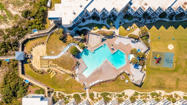 An aerial view of a resort with a large pool, multiple buildings, and a golf course. - Tommy's Bahama! in A Place At The Beach Resort on the OCEAN & the BEST pools! (Atlantic Beach)