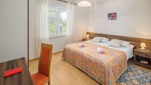 Un dormitorio ordenado con cama, mesitas de noche, una silla y una ventana con cortinas.