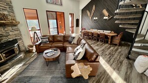 A spacious living room with a stone fireplace, leather sofa, and a dining area with a wooden table and chairs.