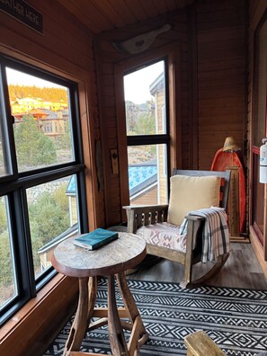 A cozy cabin interior with a rocking chair, a small table, and a view of a mountain landscape.