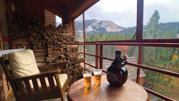 Ein gemütliches Zimmer mit Schaukelstuhl, kleinem Tisch mit zwei Biergläsern und einer Flasche, und einem großen Fenster mit Blick auf die Berge.