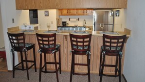 A kitchen with wooden cabinets, a central island with bar stools, and a refrigerator. - Mountainside condo in a Colorado playground! (Frisco)