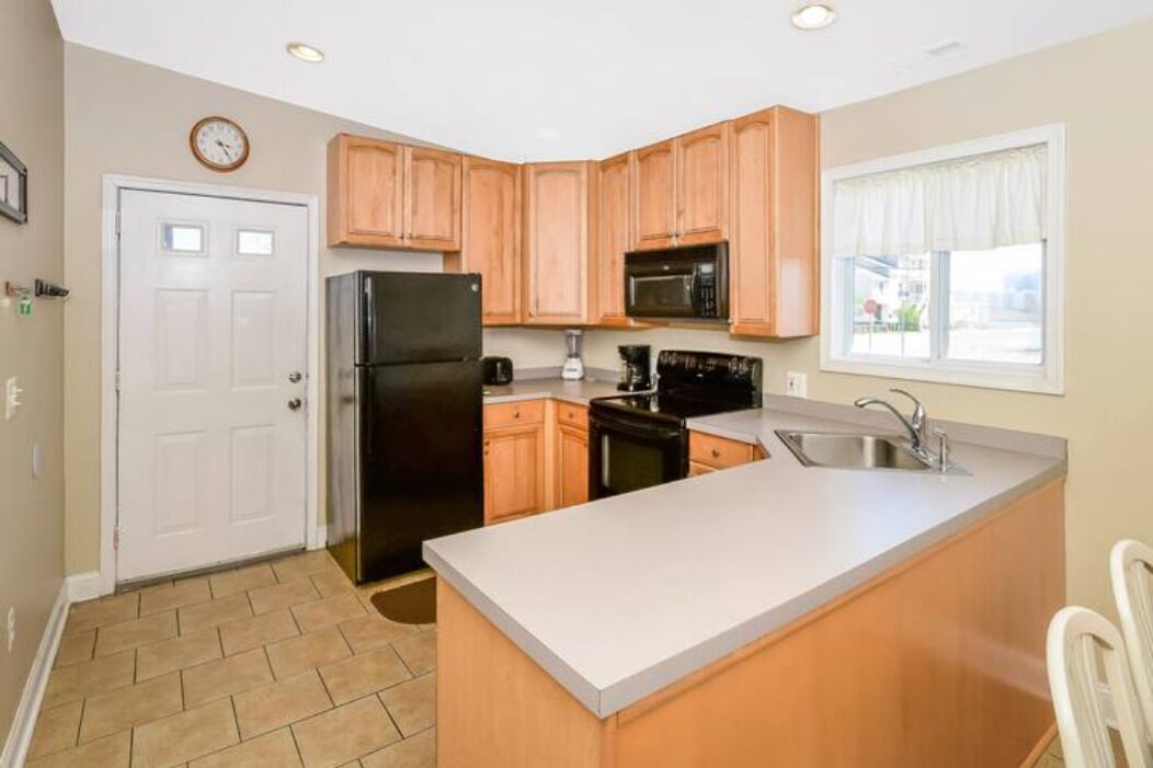 A kitchen with wooden cabinets, a black refrigerator, a microwave, and a sink.