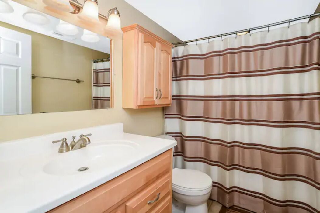 Un baño con un lavamanos blanco, tocador de madera y cortina de ducha a rayas.