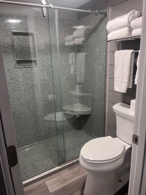 A modern bathroom with a glass-enclosed shower, a toilet, and a shelf with folded towels. - Lake front property with huge dock connected to Margaritaville (Osage Beach)