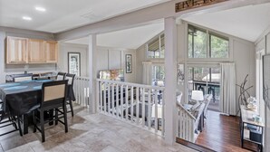 A spacious dining area with a long table and chairs, a kitchen with wooden cabinets, and a balcony with a railing. - Lake front property with huge dock connected to Margaritaville (Osage Beach)
