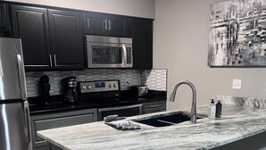 A modern kitchen with dark cabinets, stainless steel appliances, a marble countertop, and a built-in sink. - Lake front property with huge dock connected to Margaritaville (Osage Beach)