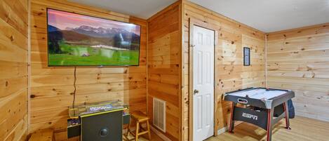 A wooden room with a television, a pool table, and a small table with a computer.