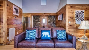 Een knus interieur van een chalet met een leren bank, houten wanden, een stenen open haard en een rustieke eethoek.