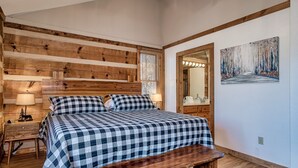 Een slaapkamer met een houten hoofdbord, een geruit sprei, een nachtkastje met lamp en een bankje.