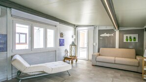 A room with a white cushioned bench, a beige sofa, and a wooden side table with a lantern. - Gorgeous home in Santa Croce Camerina (Santa Croce Camerina)
