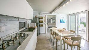 A modern kitchen with a central island, a dining area with a table and chairs, and a view through a glass door to an outdoor area. - Gorgeous home in Santa Croce Camerina (Santa Croce Camerina)