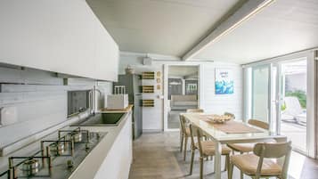 Eine moderne Küche mit Kochinsel, ein Essbereich mit Tisch und Stühlen sowie ein Ausblick durch eine Glastür in einen Außenbereich.