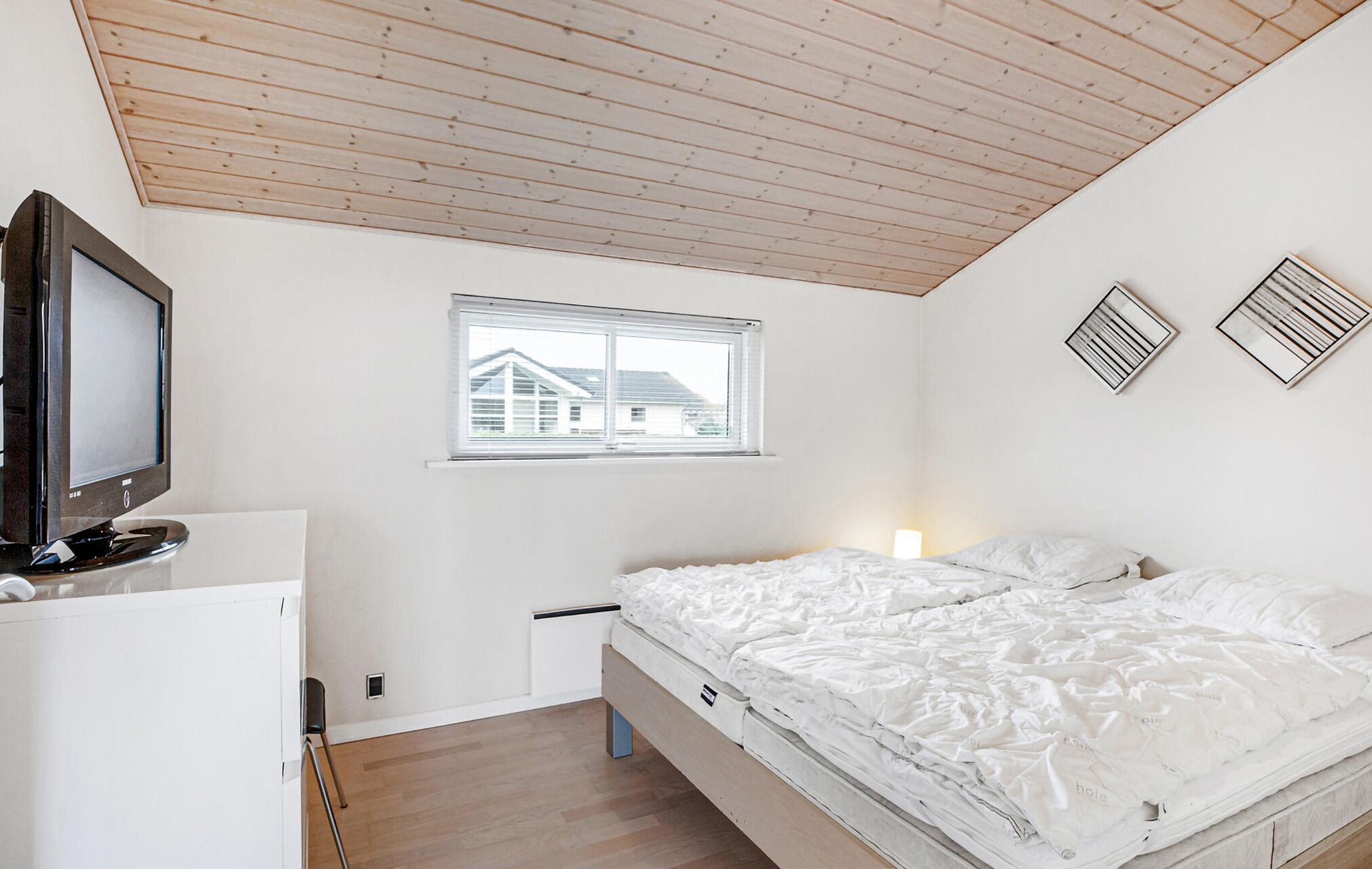 Un dormitorio con cama, televisión, ventana y techo de vigas de madera.