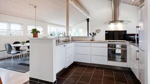 A modern kitchen with white cabinetry, a stainless steel range hood, and a large window providing natural light. - Nice home in Sydals with sauna (Sydals)