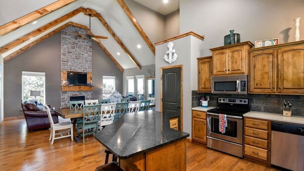 A spacious kitchen with wooden cabinets, a central island, and a stone fireplace.