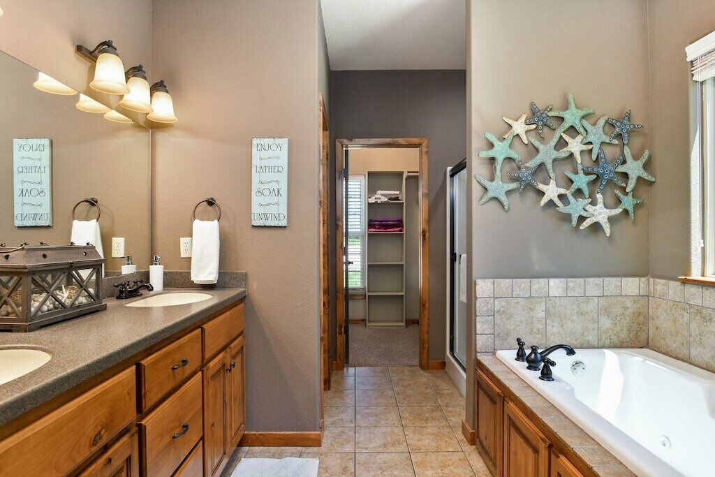A bathroom with two sinks, a bathtub, and a shower. There are decorative starfish on the wall and a mirror with light fixtures.
