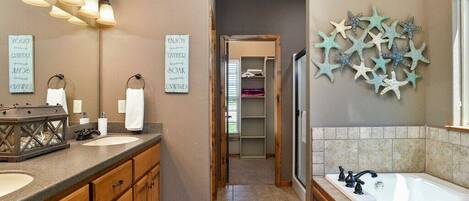 A bathroom with two sinks, a bathtub, and a shower. There are decorative starfish on the wall and a mirror with light fixtures.