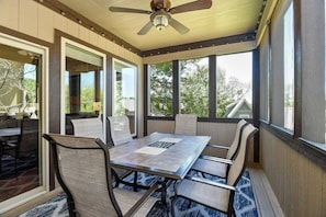 Eine überdachte Terrasse mit Tisch und Stühlen, großen Fenstern und einem Deckenventilator.