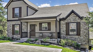 A two-story house with a stone facade, a front porch with a railing, and a clear blue sky.