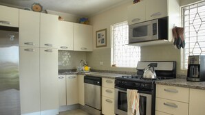 Una cocina con gabinetes blancos, lavavajillas, horno, microondas y hervidor.