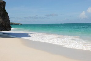 Una platja amb aigua turquesa cristal·lina, sorra blanca i un penya-segat rocos.