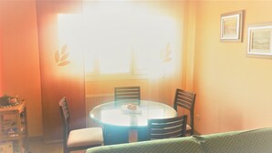 Un petit coin repas comprenant une table ronde en verre, deux chaises et une fenêtre avec un rideau.