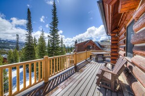 A wooden deck with a view of snow-covered mountains and pine trees. - 5 Bedroom Ski In/Out Powder Ridge Cabin (Big Sky)