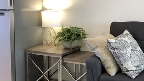 A compact living space with a modern kitchenette, a side table with a lamp, a potted plant, and a dark armchair with patterned cushions. - Studio apartment on the banks of Yellowstone River (Gardiner)