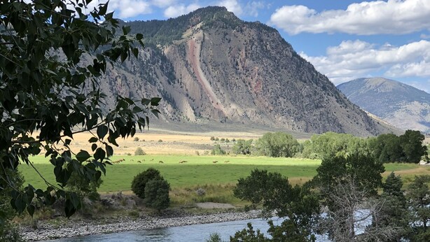 A view of a river with a mountain in the background, a grassy field, and a wooden fence in the foreground. - Studio apartment on the banks of Yellowstone River (Gardiner)