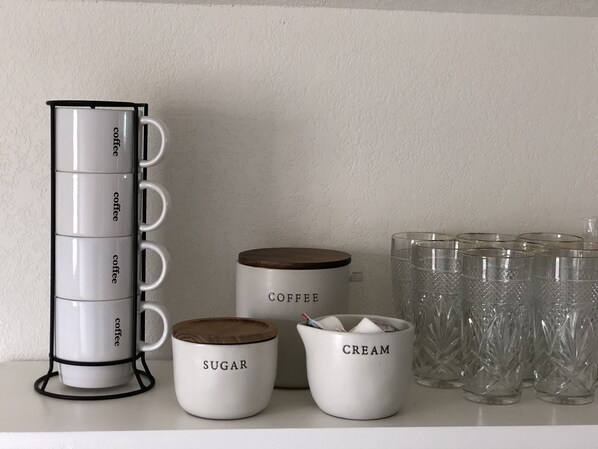 Een keukentafel met een koffiezetapparaat, suiker-en roomhouders, en een set glazen.