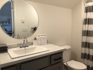 Un baño con lavamanos blanco, un espejo y artículos de aseo en el mostrador.