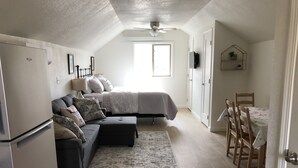 A compact, well-lit room with a bed, a sofa, a dining table, and a ceiling fan. - Studio apartment on the banks of Yellowstone River (Gardiner)