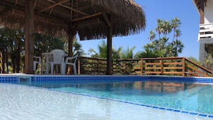 A clear swimming pool with a wooden deck and chairs, surrounded by palm trees. - La Vida Belize - Casa is a Beautiful Beach Front Home with Pool (Placencia)
