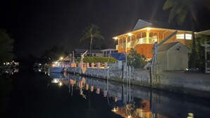 A waterfront property with a large house featuring a balcony, a small boat docked nearby, and a reflection in the water. - Fish, Swim, Relax, Party - 4bd, 3ba - 75’ Dockage & Private POOL! (Marathon)