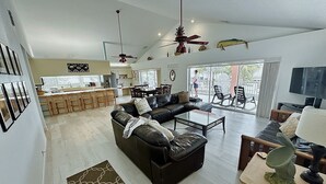 A spacious living area with a black leather sofa, a glass coffee table, and a dining area with wooden chairs. - Fish, Swim, Relax, Party - 4bd, 3ba - 75’ Dockage & Private POOL! (Marathon)