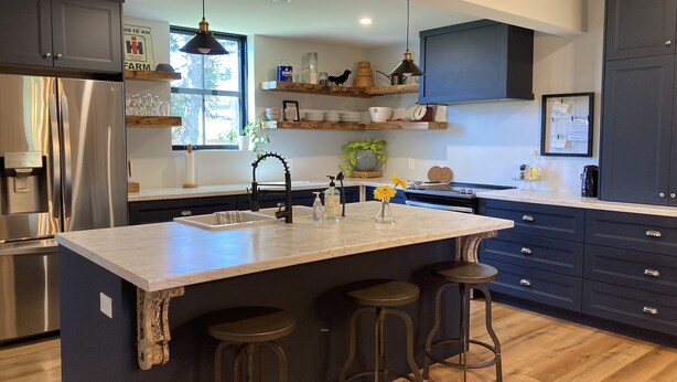 A modern kitchen with a central island, bar stools, stainless steel appliances, and wooden flooring.