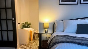 A bedroom with a bed, a nightstand, a lamp, a plant, and a door.