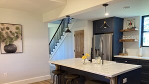 A kitchen with a marble island, bar stools, a refrigerator, and a staircase.