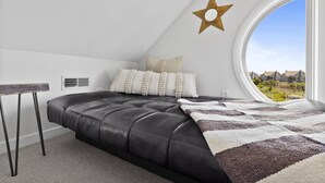 Une chambre avec une grande fenêtre, une décoration sur le thème des étoiles, un lit recouvert d’une couverture à rayures et une petite table.