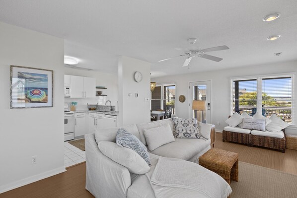 A modern living room with a sofa, a dining table, and a kitchen in the background. - Relax, unwind and have a great time at Two Beaches. (Topsail Beach)