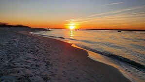 Une plage au coucher du soleil, avec un ciel dégagé, une eau calme et des empreintes de pas bien visibles dans le sable.