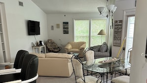 A modern living room with a sofa, armchairs, a glass coffee table, and a dining table. - Oyster Pointe Flip Flop Stop Sound-side Condo (Kill Devil Hills)