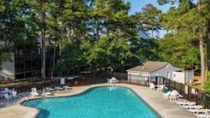A swimming pool with lounge chairs and a covered area, surrounded by trees. - Oyster Pointe Flip Flop Stop Sound-side Condo (Kill Devil Hills)