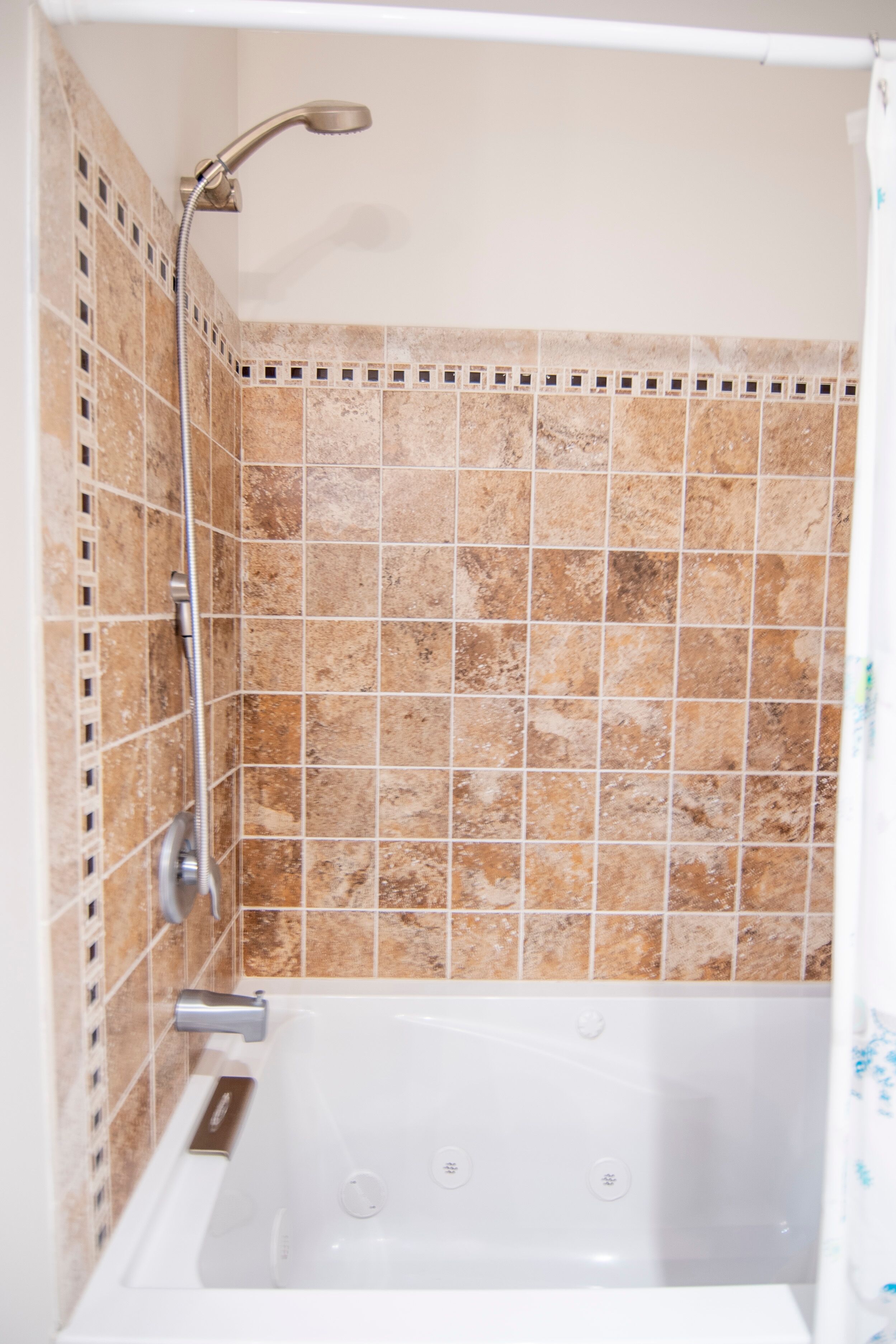 Ein Badezimmer mit Badewanne, Duschkopf und Fliesenwänden.