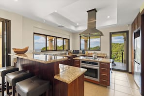Cocina moderna con una isla central, electrodomésticos de acero inoxidable y ventanas amplias con vistas al exterior.