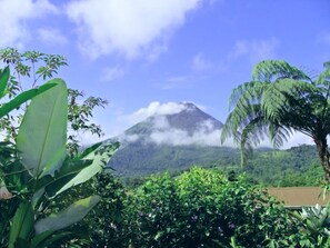 A mountain with clouds, surrounded by lush greenery and a clear blue sky.