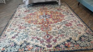 Une chambre à coucher comprenant un lit, deux lampes de chevet, un ventilateur de plafond, un tapis décoratif, une table de chevet, une commode et une fenêtre.
