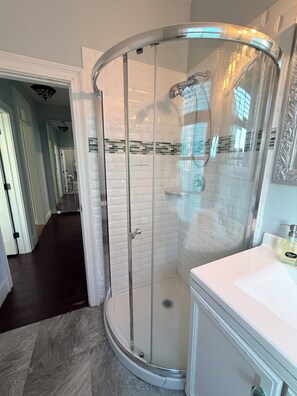 Une salle de bain moderne avec une douche Ă parois de verre, des murs recouverts de carreaux blancs et un meuble-lavabo blanc.