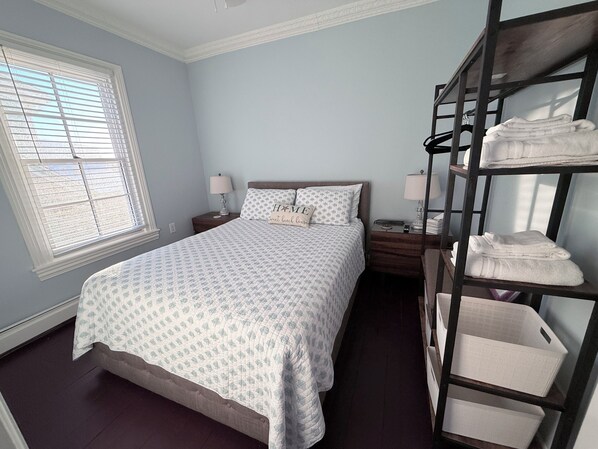A bedroom with a bed, two bedside tables, a window with blinds, and a shelf with folded towels. - 1 Block from Cape May Beach & 10 min. walking distance to mall-3rd Floor Unit (Cape May)